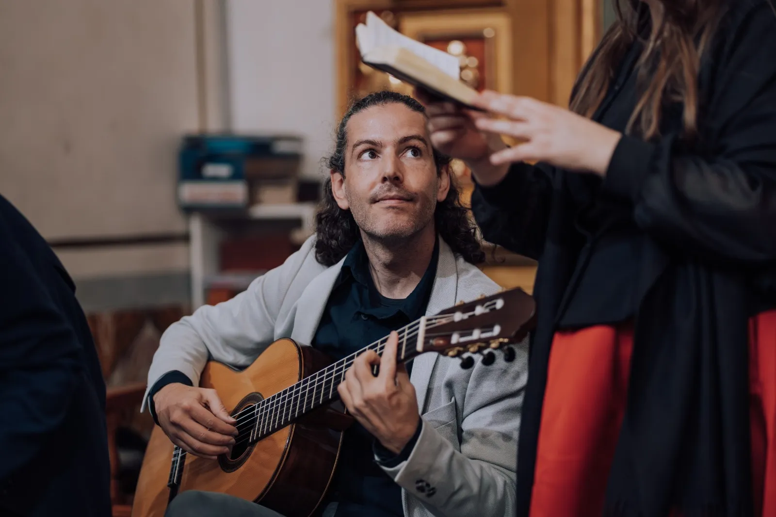 Víctor González playing classical guitar, looking up at a singer